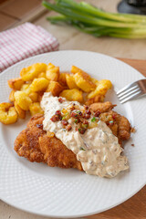 German schnitzel with sour cream bacon onion sauce and fried potatoes, on a plate. 