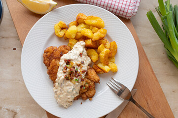 German schnitzel with sour cream bacon onion sauce and fried potatoes, on a plate. 