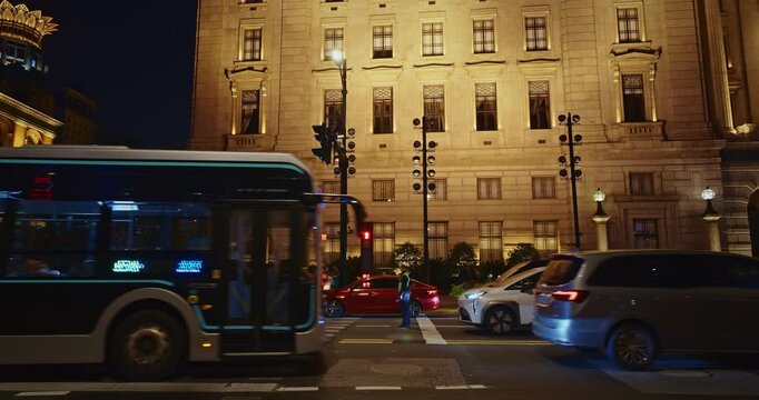 Illuminated Building Facade at Night with Traffic and Pedestrians Walking