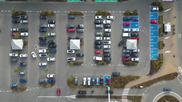 Aerial view of busy parking lot near shopping center, showcasing various parked vehicles, camera pans across scene highlighting parking dynamics and space utilization