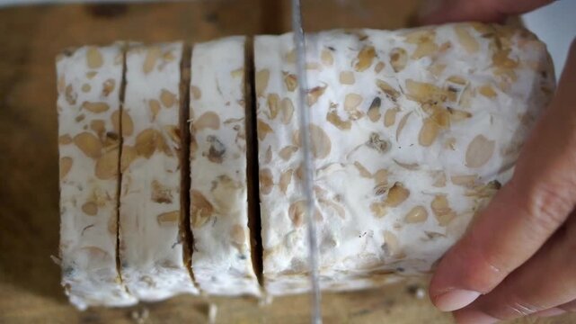 A person&rsquo;s hands slicing tempeh on a wooden cutting board for cooking preparation.