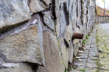 Water pipe sticks out from a stone wall next to a cobblestone path covered with fallen leaves in an urban area