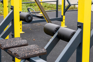 A set of outdoor gym equipment is placed in a park. The equipment features yellow and black colors with various workout areas