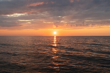 Beautiful golden sunset over the calm Baltic Sea horizon in Estonia with dramatic clouds and sunlight reflecting on the water