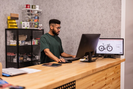Young man researching bicycle on computer in shop