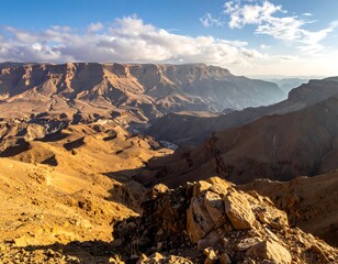 Vast panoramic vista of a rugged, canyon landscape under a partly cloudy sky. The terrain is a mix of rock and sparse vegetation