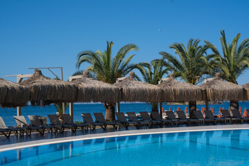 Resort area with a swimming pool, beach, and palm trees under a clear sky during daytime