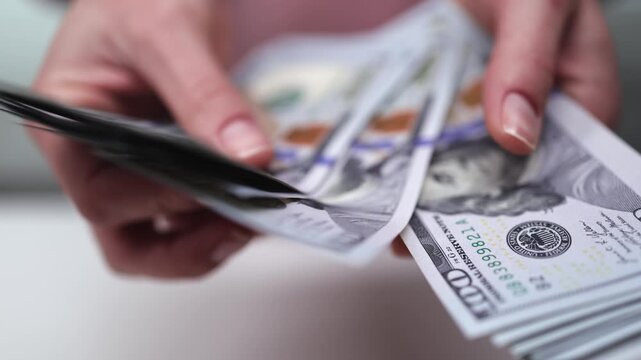 Hands count and organize stacks of cash, showcasing the detailed process of handling money, with a focus on the crisp bills and careful movements in a well-lit environment