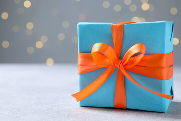 Beautiful wrapped gift on table against grey background with bokeh lights, closeup. Space for text