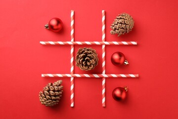Tic tac toe game made with Christmas balls and cones on red background, flat lay