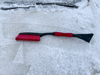 Removing snow from a car window with a brush with red bristles close-up on a sunny, frosty day. Cleaning and clearing the car from snow on a winter day. Snowfall, and a severe snowstorm in winter.
