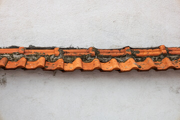 Old terracotta roof tiles on a white plaster wall, showing rustic Mediterranean architecture detail and weathered building texture