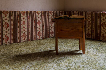 Open book resting on a small wooden table in a traditional interior with patterned fabric seating, calm reading and study atmosphere