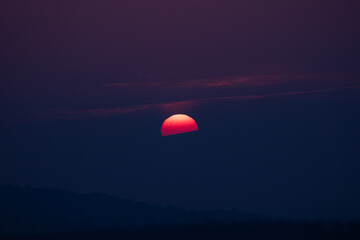 Dramatic sunset with the sun partially hidden by dark clouds, creating a moody sky and minimal atmospheric landscape