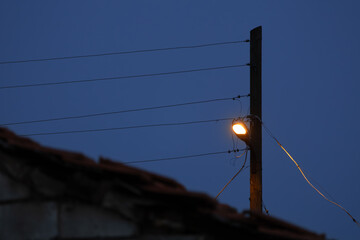 Lonely street light on a wooden utility pole at dusk with power lines against a deep blue evening sky, creating a minimal urban mood