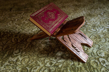 Closed Quran on a carved wooden rehal placed on mosque carpet, highlighting Islamic devotion, tradition, and quiet spiritual atmosphere
