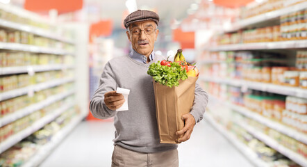 Confused elderly man holding receipt and grocery bag