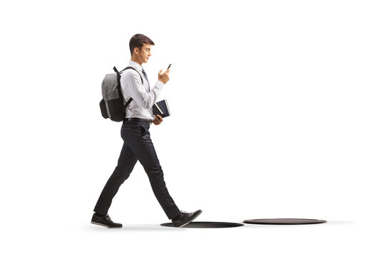 Full length profile shot of a distracted male student walking with a smartphone towards an open manhole