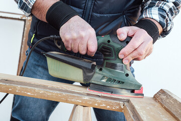 Craftsman. Adult carpenter using an electric sander to smooth an old wooden window. Construction industry, carpentry, housework do it yourself. Restoration.