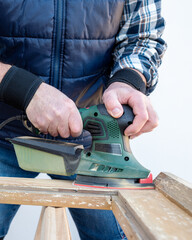 Craftsman. Adult carpenter using an electric sander to smooth an old wooden window. Construction industry, carpentry, housework do it yourself. Restoration.