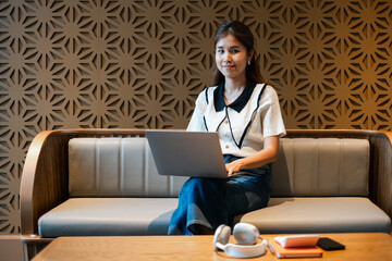 A young woman sits on a modern sofa using a laptop, surrounded by contemporary decor, representing productivity and technology.