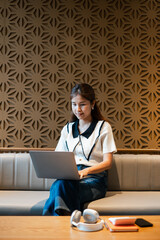 A young woman focused on her laptop in a modern lounge with a geometric wall, showcasing a blend of technology and contemporary design.