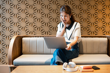 A young woman looks surprised while using a laptop on a modern sofa, set against a stylish geometric wall design.