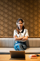Woman wearing headphones sitting on a sofa with a laptop, set against a modern geometric wall design.