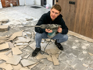 Removing a concrete floor with a hand hammer. Concrete rubble on the construction site of a house. Destruction of old tiles. Male construction removes the old tile from the floor with a hammer drill.