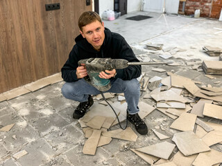 Removing a concrete floor with a hand hammer. Concrete rubble on the construction site of a house. Destruction of old tiles. Male construction removes the old tile from the floor with a hammer drill.