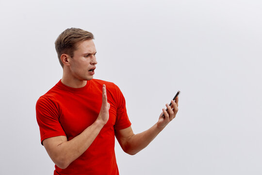 upset young caucasian man wearing red t-shirt holding smartphone reject cyber security threat individual isolated on light background technology concept - Powered by Adobe