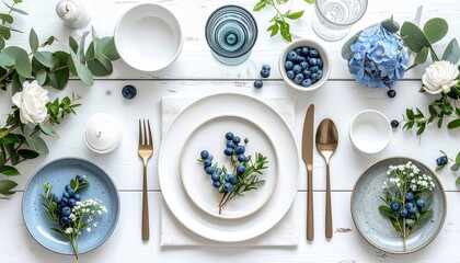 Elegant table setting with white & blue tableware, florals, and berries on a white wood surface
