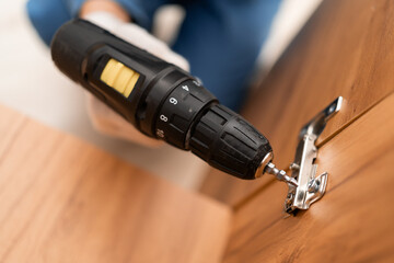 Assembly furniture. Close-up of handyman using electric drill for fixing hinges. Carpentry