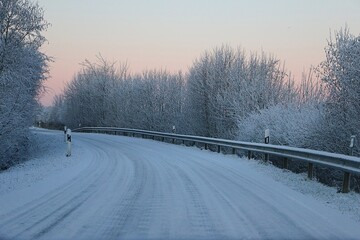 Small curved snow-covered country road with trees on the side early in the morning