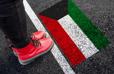 a woman with a boots standing on asphalt next to flag of Kuwait and border
