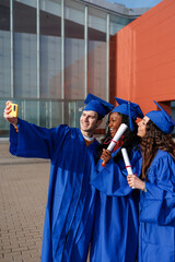 Happy multiethnic graduates wearing blue caps and gowns, smiling and holding diplomas