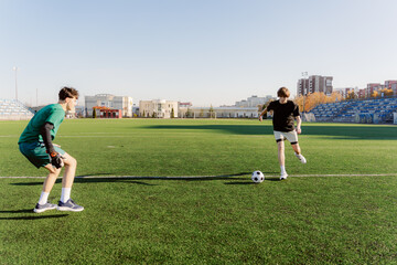 Two boys enjoy a lively soccer practice on a well-maintained field. One boy prepares to shoot while the other gets ready to defend under clear blue skies.