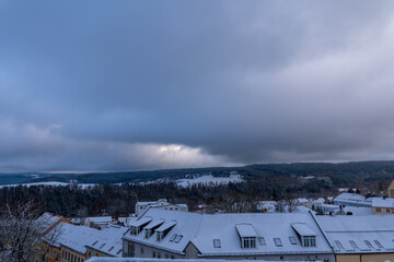 Snowy rooftops under a dramatic sky with clouds rolling in, capturing winter's quiet beauty in a serene landscape