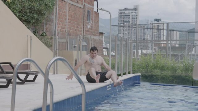 slow motion video of a man in his mid 30s standing up from the edge of a swimming pool and walking out of frame, the subject is a light skinned latino man with an overweight body type