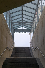 Sturdy stairs lead upward through a modern glass structure toward a cloudy sky