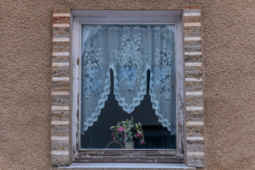 Delicate lace curtains filter soft light into a quaint window adorned with flowers in a cozy, rustic setting