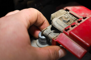 A man's hand carefully installs or removes a metal terminal from a car battery under the hood of a vehicle. This close-up shot demonstrates the technical process of maintaining the car's electrical sy
