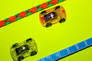 Bright translucent toy cars and flexible anti-stress tracks arranged on a neon lime green background. This dynamic composition with contrasting colors is perfect for visualizing children's entertainme