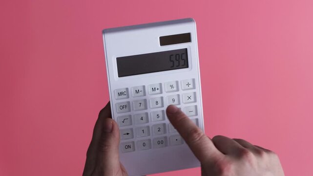 Close-up of hands using a white calculator with a pink background