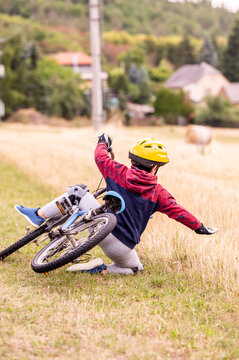 little boy riding a bike with a helmet and protection pads and falling from a bike into the grass