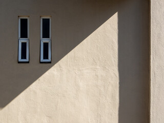Two aluminium rectangular glass awning window frame on a beige stone cement wall with diagonal shadow.