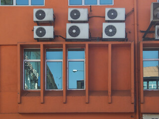 Orange building exterior wall with rectangle glass casement window and a split unit air conditioning unit mounted on the walll,