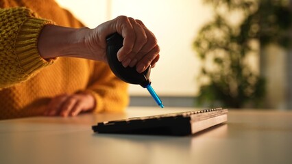 A person uses an air blower to clean dust from a computer keyboard in a well lit office environment.