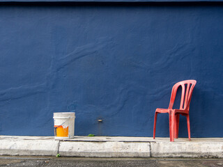 Dark blue uneven surface wall with a red  plastic chair and a white plastic pail bucket.