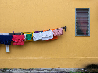 Yellow wall with a rectangle louver glass window and a clothesline with hanging clothes drying laundry.